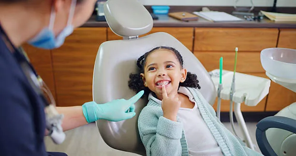 Petite fille souriante montrant ses dents au dentiste lors de sa première visite