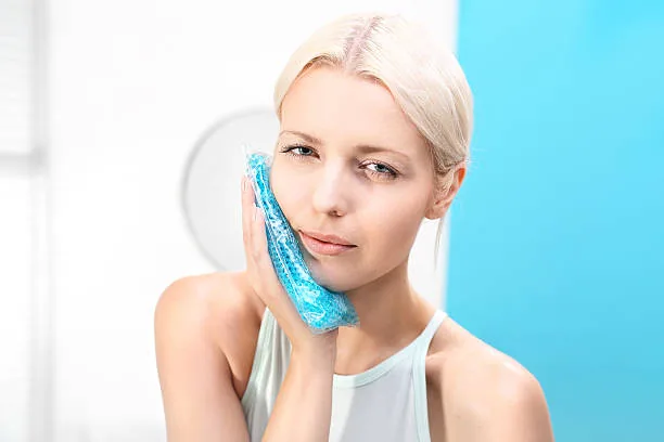 Femme appliquant une compresse froide sur la joue en cas de gonflement dentaire